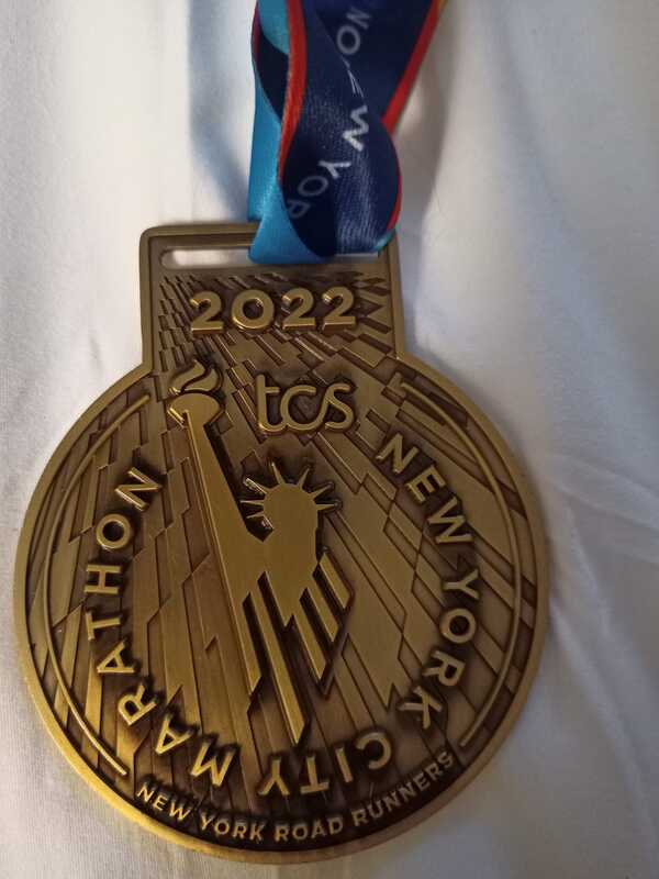 A photo of the New York marathon medal. It has the text of 2022 at the top, an image of the statue of liberty in the middle with the words of New York City marathon surrounding it