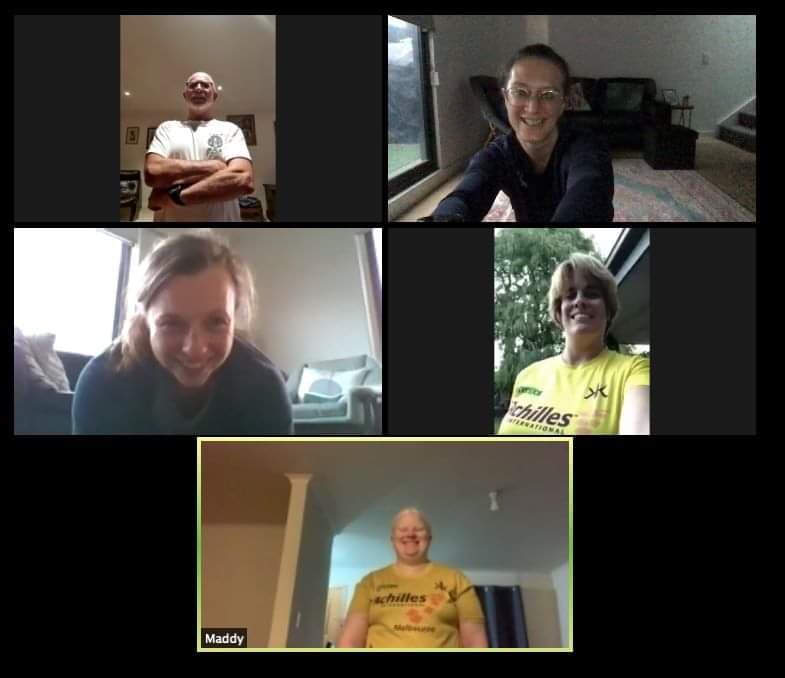 A screen shot of a video conference with five participants: a man in a white t shirt with his arms crossed, Sarah in a black top in an indoor space, a lady smiling down at her camera from an indoor space, a lady with an Achilles top in an outdoor space smiling down an her camera, another lady in an Achilles top in a darker indoor space smiling at her camera.