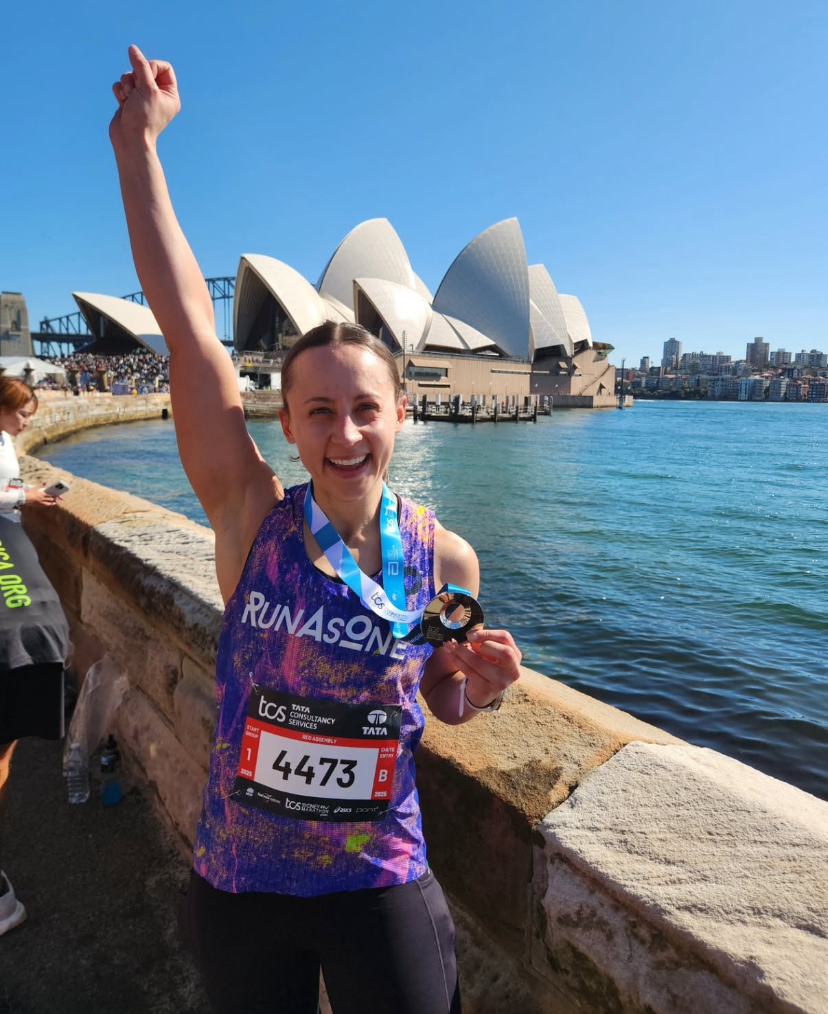 Bruna standing holding her Sydney Marathon Medal with Opera House in the background